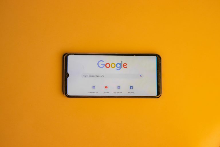 Smartphone displaying Google search page on a vibrant yellow background.