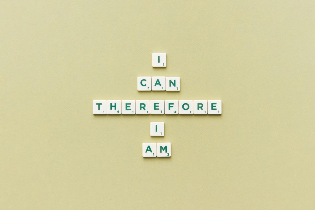 Inspirational phrase 'I Can Therefore I Am' arranged using Scrabble tiles on a green background.