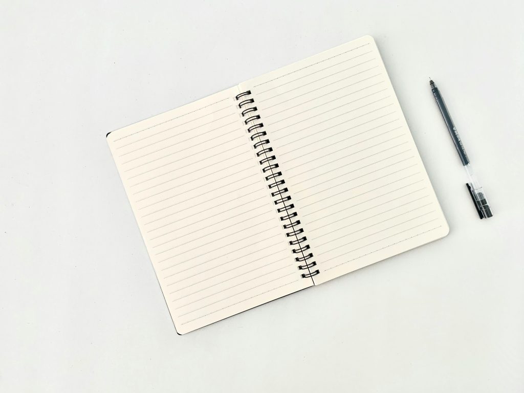 Top view of an open lined notebook and a black pen on a white background.